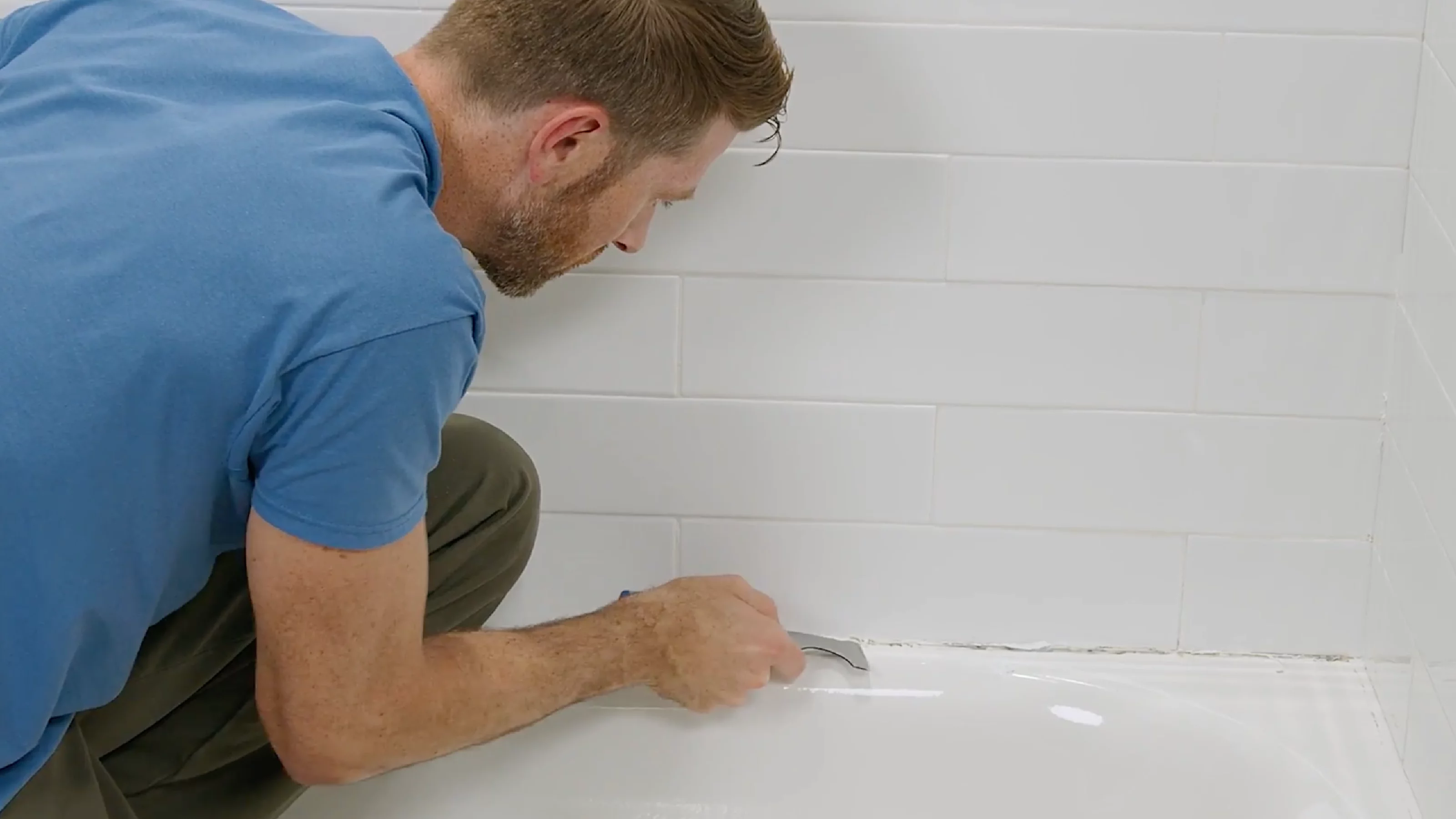 A worker using a tool to remove old silicone from a shower